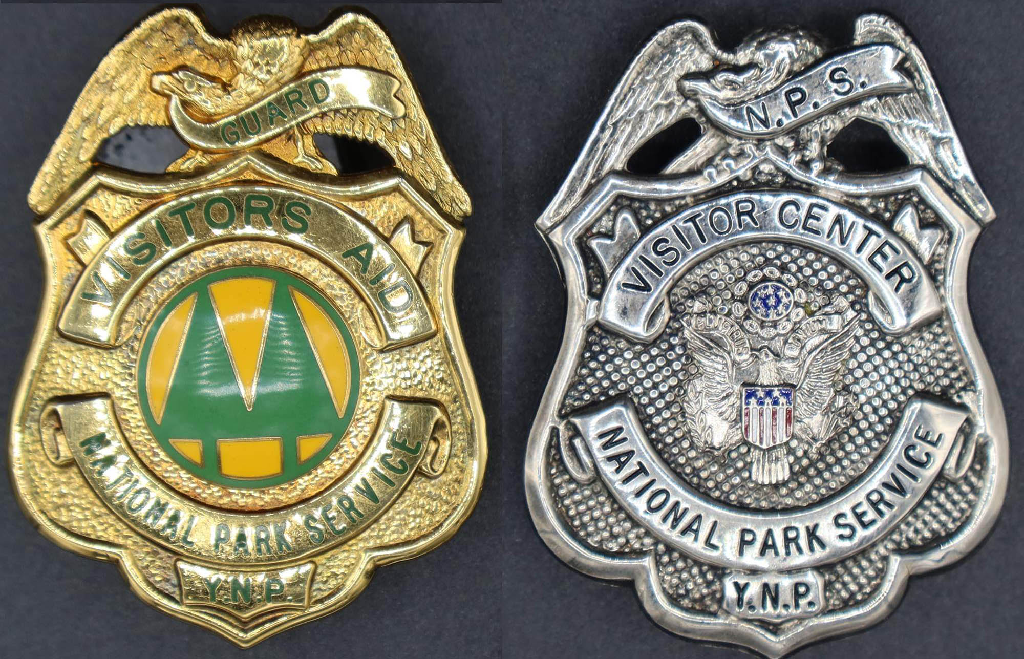 Gold visitor’s aid badge with round seal in middle with green trees on yellow. Silver Visitor Center badge with eagle with red and blue flag in middle.